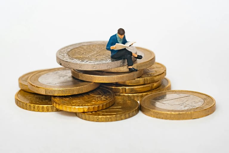 Miniature figure reading a newspaper on a stack of coins